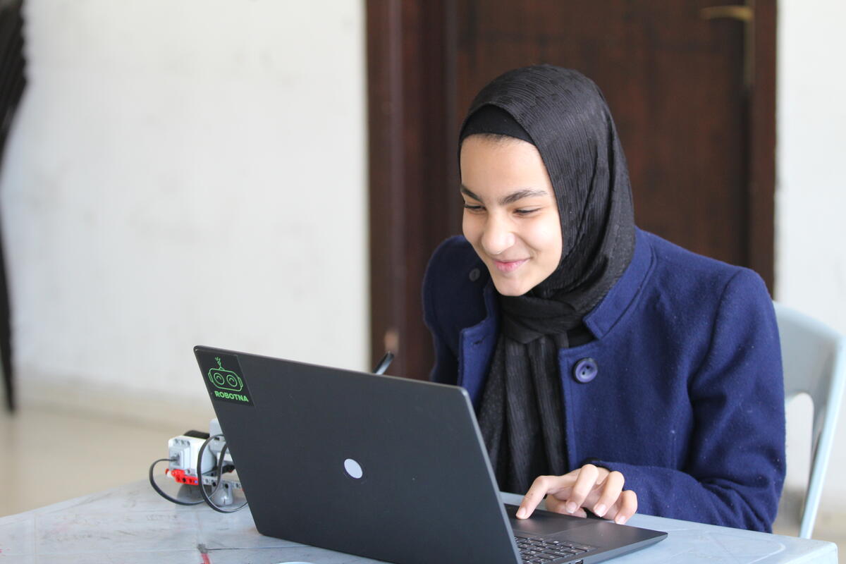 Persona giovane che guarda lo schermo di un computer e usa il trackpad, seduta sul banco di un'aula.