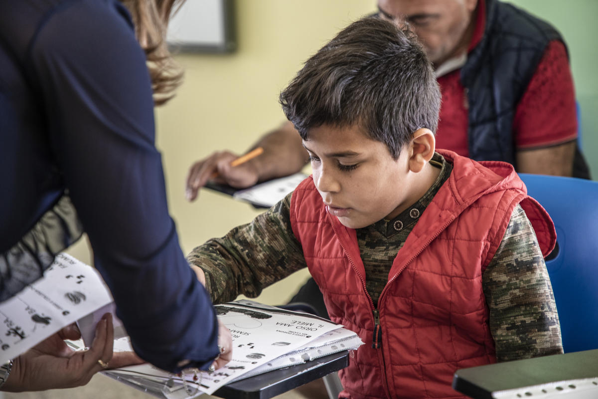 Bambinə a scuola, sedutə su una sedia mentre legge delle schede didattiche.
